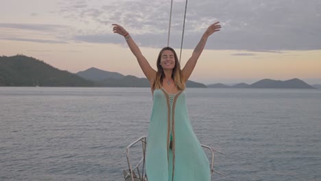 Carefree-Woman-Standing-And-Raising-Hands-In-The-Air-On-Deck-Of-Boat-With-Sunset-Sky-In-Background