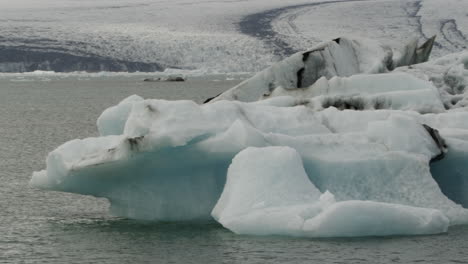 Toma-Panorámica-Suave-A-Través-De-La-Laguna-Jokulsarlon-Y-Los-Icebergs-Glaciales-Que-Se-Derriten,-Signos-Del-Calentamiento-Global-Y-El-Cambio-Climático