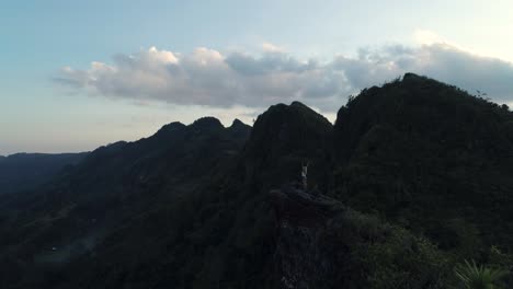 Woman-with-hands-in-air-carefree-watching-sunset-from-Kandungaw-peak,-aerial