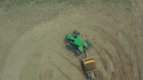 Luft-Von-Oben-Nach-Unten-Eines-Grünen-Traktors,-Der-Erde-Mit-Bodenbewegungsgeräten-Transportiert