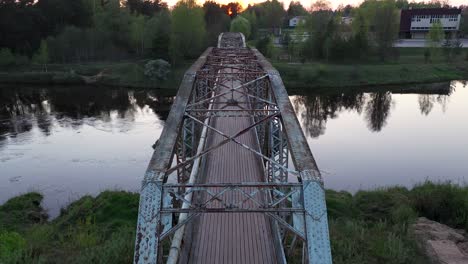 Pedestrian-bridge-over-river-Gauja-at-evening-time,-low-angle-fly-over