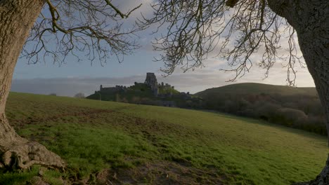 Slow-zoom-in-shot-of-Corfe-Castle-framed-by-trees-in-the-early-morning-light
