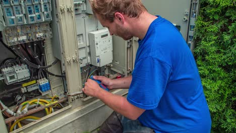 Young-man-cutting-electrical-wires-in-front-of-electric-cupboard