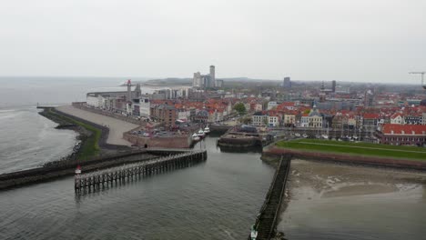Aerial-backward-shot-of-a-pier-with-waterfront-buildings-and-tower-and-a-stunning-panorama-of-the-city-of-Vlissingen,-the-Netherlands