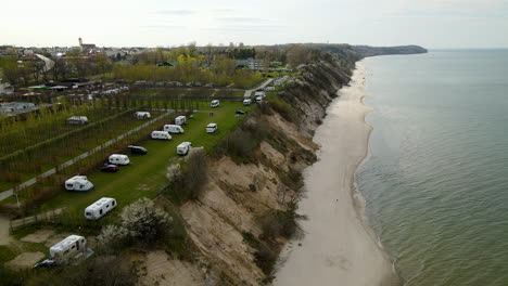 Aerial-drone-flies-along-the-camper-trailers-parking-lot-area-located-on-the-cliff-shore-of-Baltic-sea-daytime-summer-in-Chlapowo,-Poland