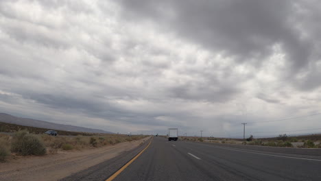 Driving-along-a-highway-through-the-Mojave-Desert-as-the-overcast-sky-threatens-rain-during-a-drought-year---point-of-view