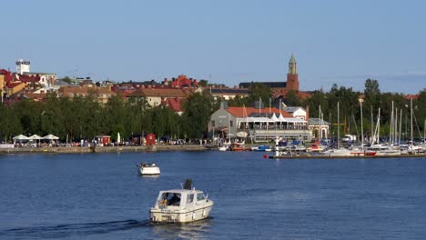 Idyllic-landscape-of-a-boat-cursing-toward-the-historical-harbor-town-on-a-sunny-day-in-Östersund-Sweden