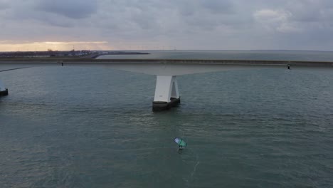 Luftumlaufbahn-über-Einem-Mann,-Der-Auf-Einem-Tragflächenflügel-Reitet,-Der-In-Der-Nähe-Der-Längsten-Brücke-Der-Zeelandbrug-In-Den-Niederlanden-Fliegt
