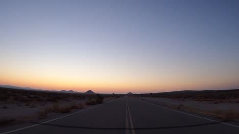 Driving-through-the-Mojave-Desert's-on-a-lonely-road-during-a-picturesque-sunset---point-of-view