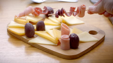 wooden-board-with-cheeses,-ham-and-olives