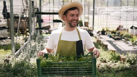 Joyful-adult-male-gardener-in-apron-carries-plants-in-a-box
