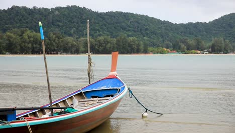 Thailändisches-Longtail-boot,-Das-Mit-Einem-Seil-Am-Strand-Entlang-Auf-Der-Insel-Koh-Lanta-In-Thailand-Mit-Wasser-Und-Wellen-Verankert-Ist