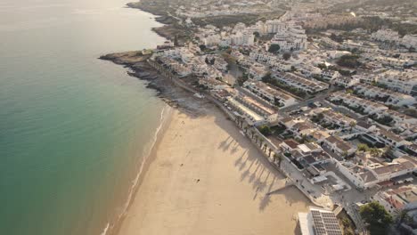 Aerial-truck-shot-over-the-costal-village-of-Praia-Da-luz-on-the-south-coast-of-Portugal,-showing-the-sandy-beaches-on-a-bright-sunny-day