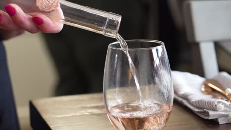 Rose-Wine-Poured-into-Stemless-Wine-Glass-and-Picked-Up-from-Table-to-be-Served,-Close-up-of-Woman’s-Hand-Wearing-Pink-Nail-Polish-and-Kitchen-Napkin-in-Background,-White-and-Golden-Red-Color