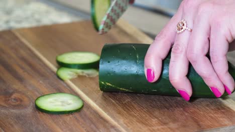 Woman-Chopping-Cucumber-into-Thin-Slices-Close-Up-on-Wooden-Cutting-Board-with-Small-Knife-Decorated-with-Flowers,-Hands-with-Pink-Nail-Polish