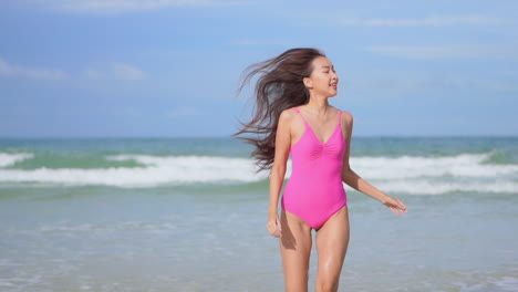 Pretty-young-woman-wearing-pink-one-piece-swimwear-running-towards-the-camera-with-strong-ocean-waves-in-the-background