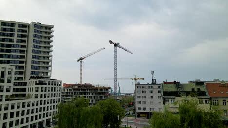 Aerial-view-of-cranes-on-construction-site-in-polish-residential-area-with-blocks-and-apartments-during-cloudy-day
