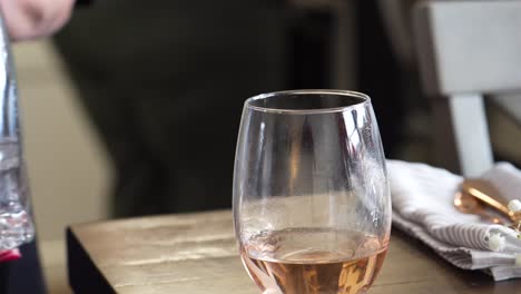Der-Server-Nimmt-Schnell-Ein-Glas-Rosenwein-In-Einem-Stiellosen-Weinglas-Auf,-Nachdem-Er-Das-Gießen-Aus-Der-Weinflasche-Beendet-Hat,-Nahaufnahme-Der-Hand-Mit-Rosa-Nagellack-Und-Serviette-Im-Hintergrund,-Weiße-Und-Goldrote-Farbe