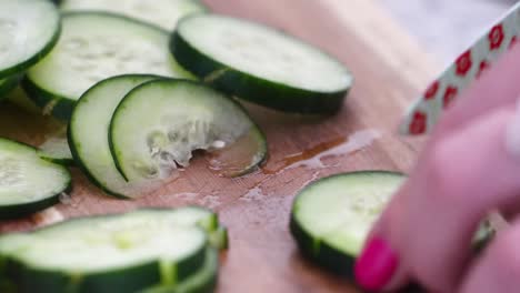 Woman-Chopping-Cucumber-Slices-into-Cubes-and-Chunks,-Close-Up-on-Wooden-Cutting-Board-with-Small-Knife-Decorated-with-Flowers,-Hands-with-Pink-Nail-Polish