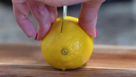 Woman-Slicing-Yellow-Lemon-In-Half-Close-Up-on-Wooden-Cutting-Board-with-Small-Knife-Decorated-with-Flowers,-Hands-with-Pink-Nail-Polish