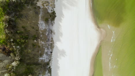 Aerial-shot-looking-down-over-bright-white-sand-beach-with-green-ocean-water-on-Baltic-Sea