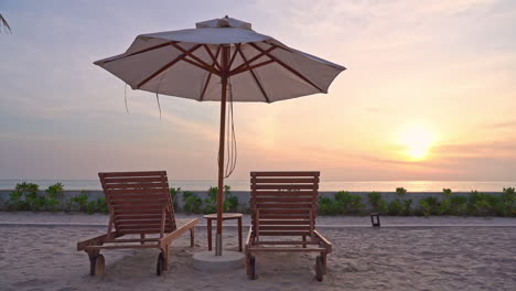 Sonnenschirm-Und-Zwei-Liegestühle-Am-Strand-Mit-Meer-Im-Hintergrund-Bei-Sonnenuntergang
