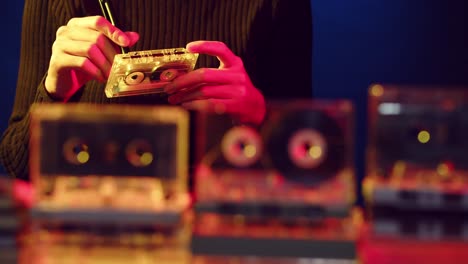 Woman's-hands-are-seen-winding-the-tape-on-a-vintage-cassette-with-a-display-of-cassettes-in-the-foreground---sliding-view-with-focus-on-the-woman