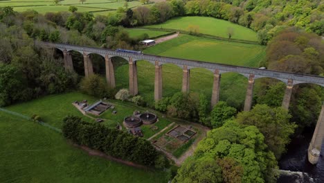 Aerial-view-following-narrow-boat-on-Trevor-basin-Pontcysyllte-aqueduct-crossing-in-Welsh-valley-countryside-reveal-orbit-left