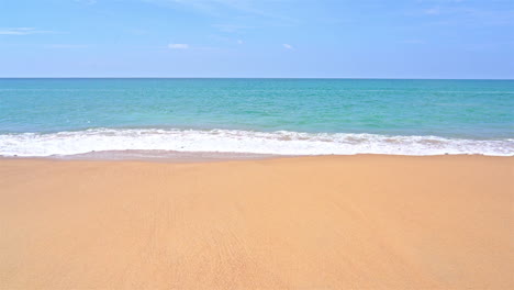 Static-shot-of-the-ocean-with-calm-waves-reaching-the-shore-of-a-white-sand-beach-on-a-tropical-island-during-bright-sunny-day