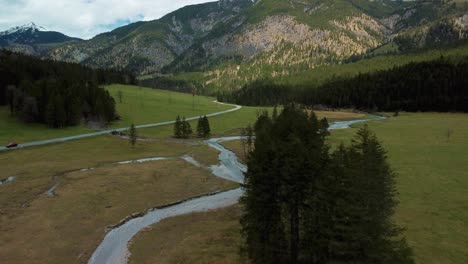 Aerial-flight-along-a-scenic-mountain-river-with-fresh-blue-water-in-the-Bavarian-Austrian-alps-on-a-cloudy-day,-flowing-down-a-riverbed-along-trees,-rocks,-forest-and-hills-seen-from-above-by-drone