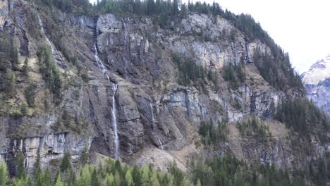 Drohnenflug-über-Ein-Wunderschönes-Alpental,-Wasserfälle-Und-Hohe-Schneebedeckte-Berge
