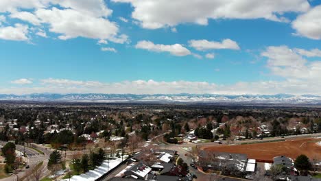 A-drone-pan-over-a-Denver-suburb,-snow-capped-mountains-on-the-horizon