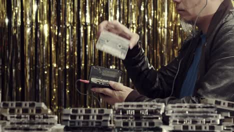 A-man-plays-and-checks-copies-of-vintage-cassettes-with-a-cassette-player-and-headphones---gold-tinsel-background