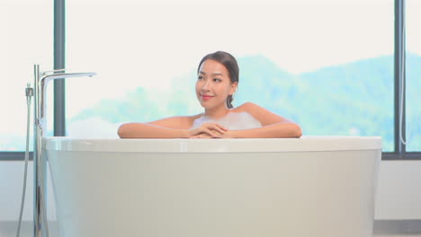 A-pretty-young-woman-in-a-bubble-bath-leans-on-the-edge-of-her-spa-like-bathtub