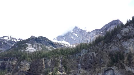 Drohnenflug-über-Ein-Wunderschönes-Alpental,-Wasserfälle-Und-Hohe-Schneebedeckte-Berge