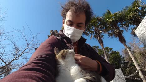Young-male-petting-cat-while-wearing-facemask-during-corona-crisis