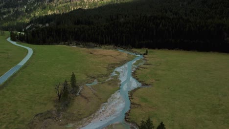 Drone-flight-along-a-scenic-mountain-river-with-fresh-blue-water-in-the-Bavarian-Austrian-alps-on-a-cloudy-day,-flowing-down-a-riverbed-along-trees,-rocks,-forest-and-hills-seen-from-above-by-drone
