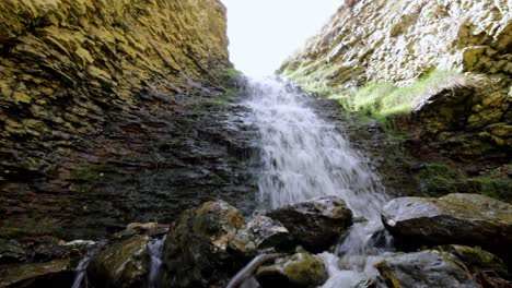 Agua-Que-Fluye-Sobre-Una-Cascada-Que-Se-Estrella-Contra-Rocas-Pulidas