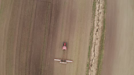 Aerial-view-from-drone-looking-down-on-tractor-towing-machine-in-field