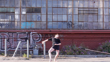 Woman-Interpretative-Dancing-Barefoot,-Pan-Down-Abandoned-Glass-Window-Warehouse,-Wide-Shot