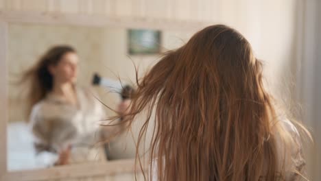 Beautiful-young-woman-blow-drying-her-hair-in-front-of-a-mirror