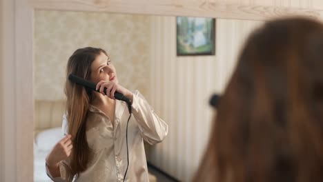 Young-woman-in-the-mirror-straightens-with-a-curling-iron