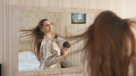 pretty-young-woman-in-the-mirror-dries-her-hair-with-a-hair-dryer