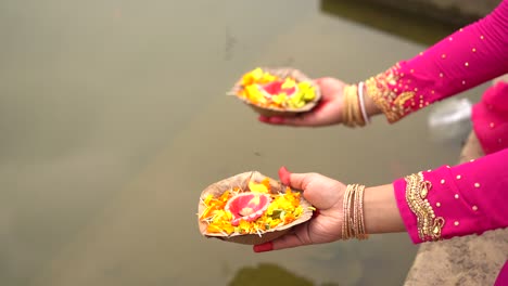 Closeup-of-hands-of-unrecognized-women-holding-diya-for-aarti-near-river-water,-prayer-for-indian-gods