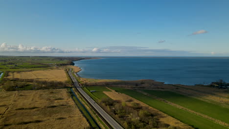 Aerial-view-showing-sea-road-with-driving-cars-surrounded-by-agricultural-fields-in-Puck-during-sunny-day,Poland