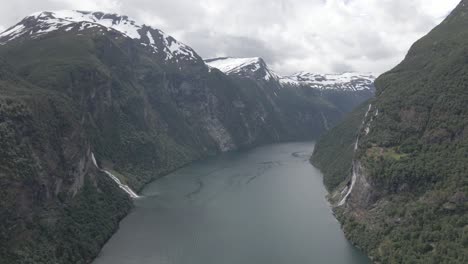 Vista-Aérea-Del-Majestuoso-Fiordo-De-Geiranger-Con-Cumbres-Nevadas-Y-Cascadas,-Noruega