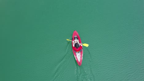 Boy-wearing-a-red-shirt-and-a-cap-rowing-in-his-kayak-over-green-waters