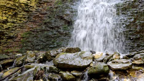 Ein-Wasserfall,-Der-Auf-Polierte-Felsen-Mit-Bunten-Sedimenten-In-Der-Klippenwand-Stürzt