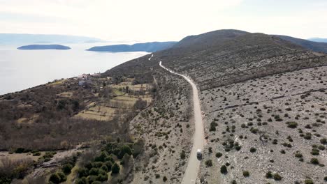 Aerial-view-of-a-lone-motorhome-driving-on-road-by-Adriatic-coastline,-Cres,-Croatia