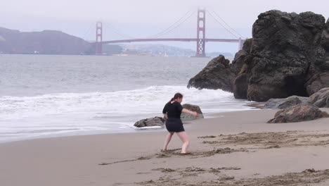 Woman-Does-Dramatic-and-Emotional-Interpretive-Dance-on-the-Beach,-Golden-Gate-Bridge-in-Background